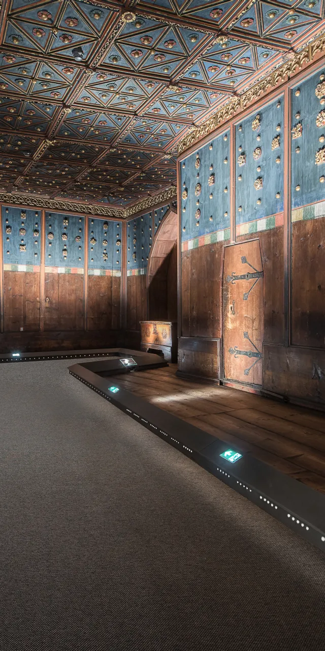 Historischer Holzraum mit blauer Wandverkleidung, verziertem Deckengewölbe und geschnitzter Truhe